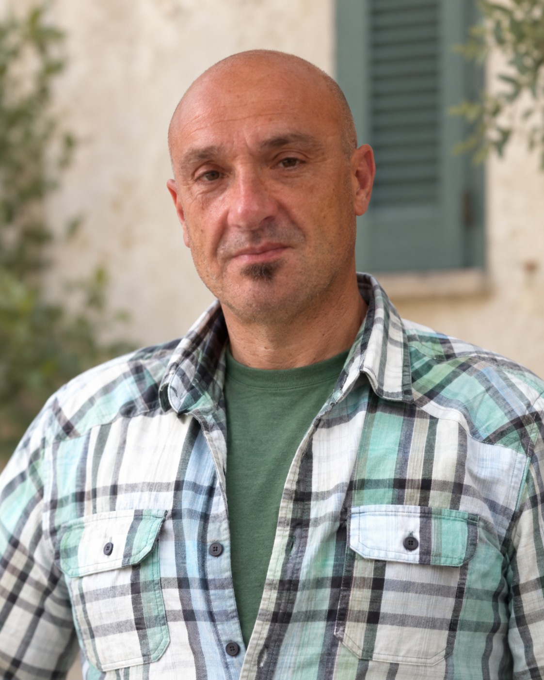 Ritratto di Cesare Micheloni con camicia a quadri, su uno sfondo tenue avorio e verde salvia.